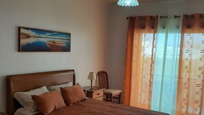 Una camera da letto con un letto, un comodino, una sedia, una lampada, un quadro e una finestra con tende.