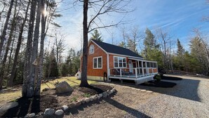 A single-story wooden cabin with a porch, surrounded by a gravel driveway and a stone border. - Entire Home in Carthage, ME (Carthage)