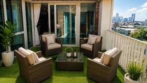 Een balkon met rieten meubilair, een glazen tafel en plantenpotten.
