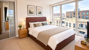 Een moderne slaapkamer met een groot bed, twee bedlampjes, uitzicht op de stad door grote ramen en een stadsbeeld buiten.