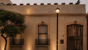 Fachada de edificio con una puerta de madera grande, una ventana con barandilla metálica y un farol de calle.