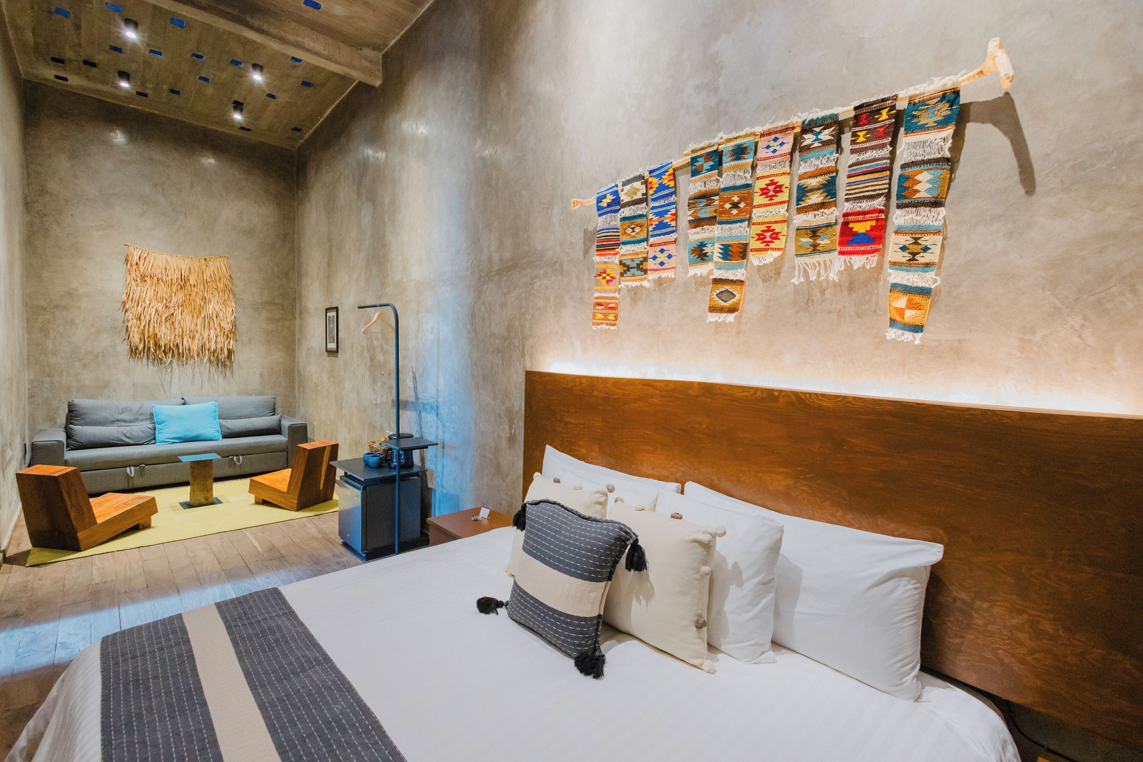 Una camera d'hotel moderna con un letto grande, un divano, un tavolino e una parete decorata con tessuti colorati.