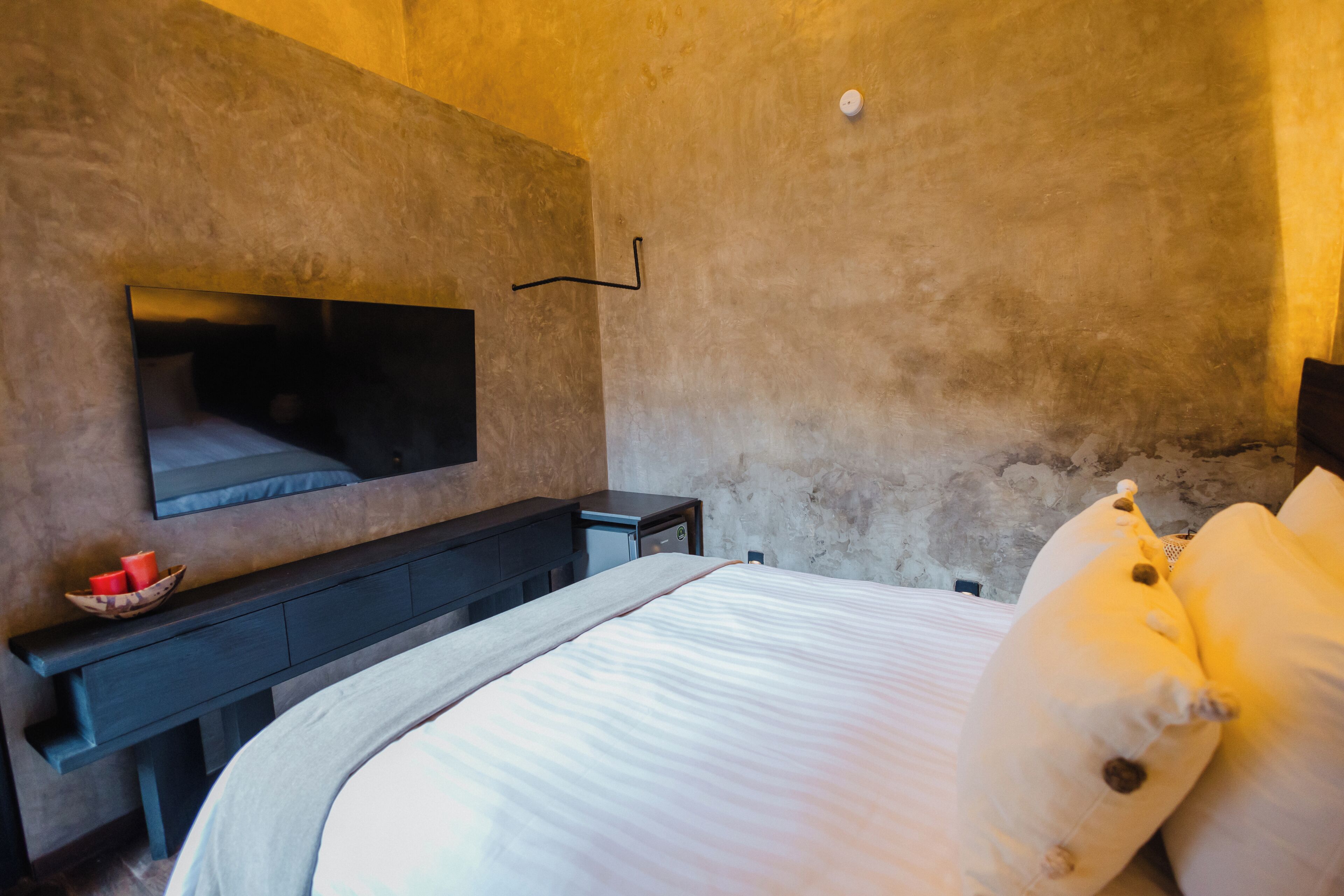 A bedroom with a bed, a TV mounted on the wall, a small table with a bowl, and a nightstand.