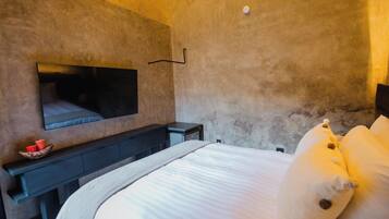 A bedroom with a bed, a TV mounted on the wall, a small table with a bowl, and a nightstand.