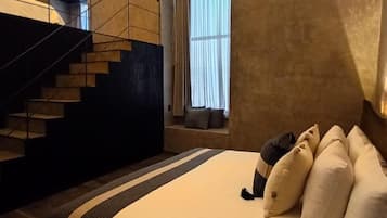 Un dormitorio con cama, almohadas, una ventana con cortinas y una escalera.