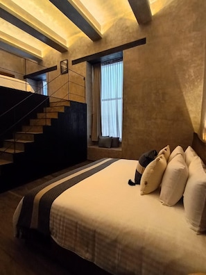 Un dormitorio con cama, almohadas, una ventana con cortinas y una escalera.
