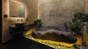Un baño moderno con una gran pieza de roca como elemento central, un lavabo y un espejo.