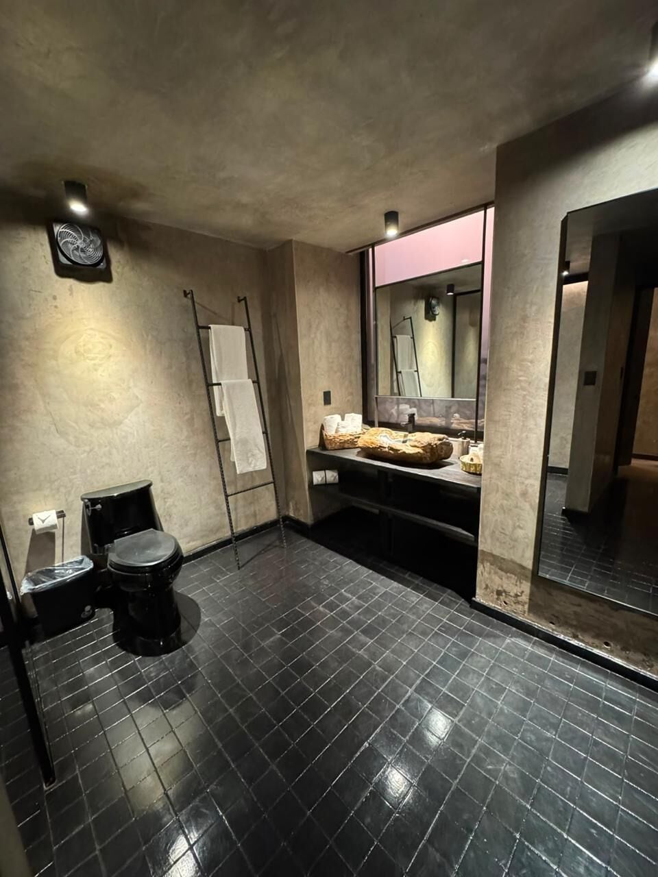 A modern bathroom with a black tiled floor, a toilet, a sink with a mirror, and a towel rack.