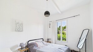 Ein Schlafzimmer mit Bett, Nachttisch, Lampe und einem Spiegel auf einem Gestell.