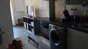 Eine kompakte Küche mit Waschmaschine, Esstisch und Fernseher.