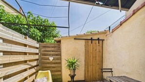 Eine Terrasse mit einer hölzernen Bank, einem gelben Stuhl, einem Blumentopf und einem gefliesten Boden.