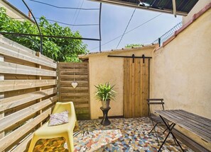 A patio with a wooden bench, a yellow chair, a potted plant, and a tiled floor. - The Musette Nest (Avignon)