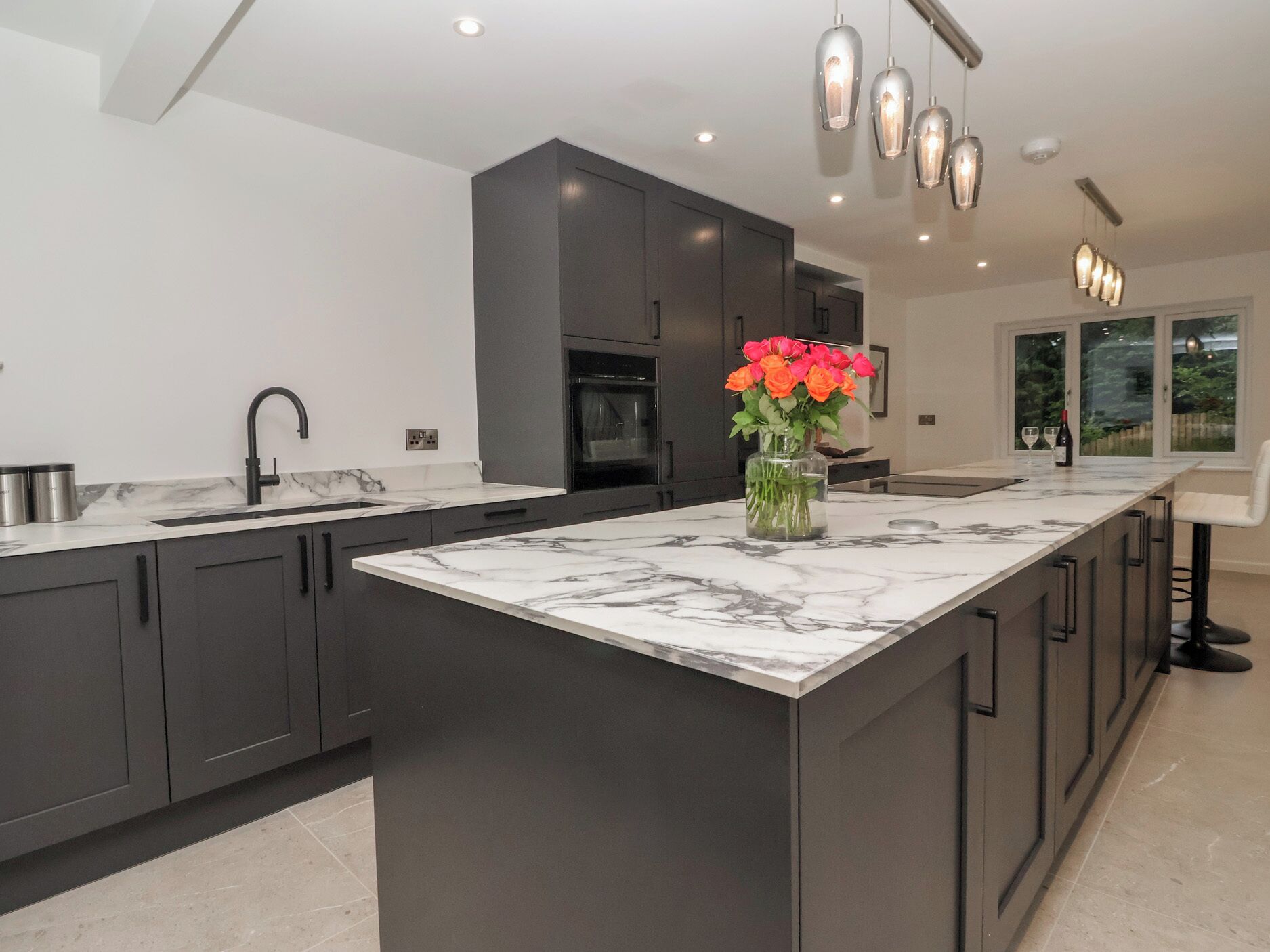 A modern kitchen with a marble island, dark cabinetry, and a vase with flowers.