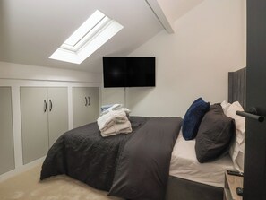 A bedroom with a bed, a flat-screen TV mounted on the wall, and a skylight above the bed. - Wood Cottage (Skipton)