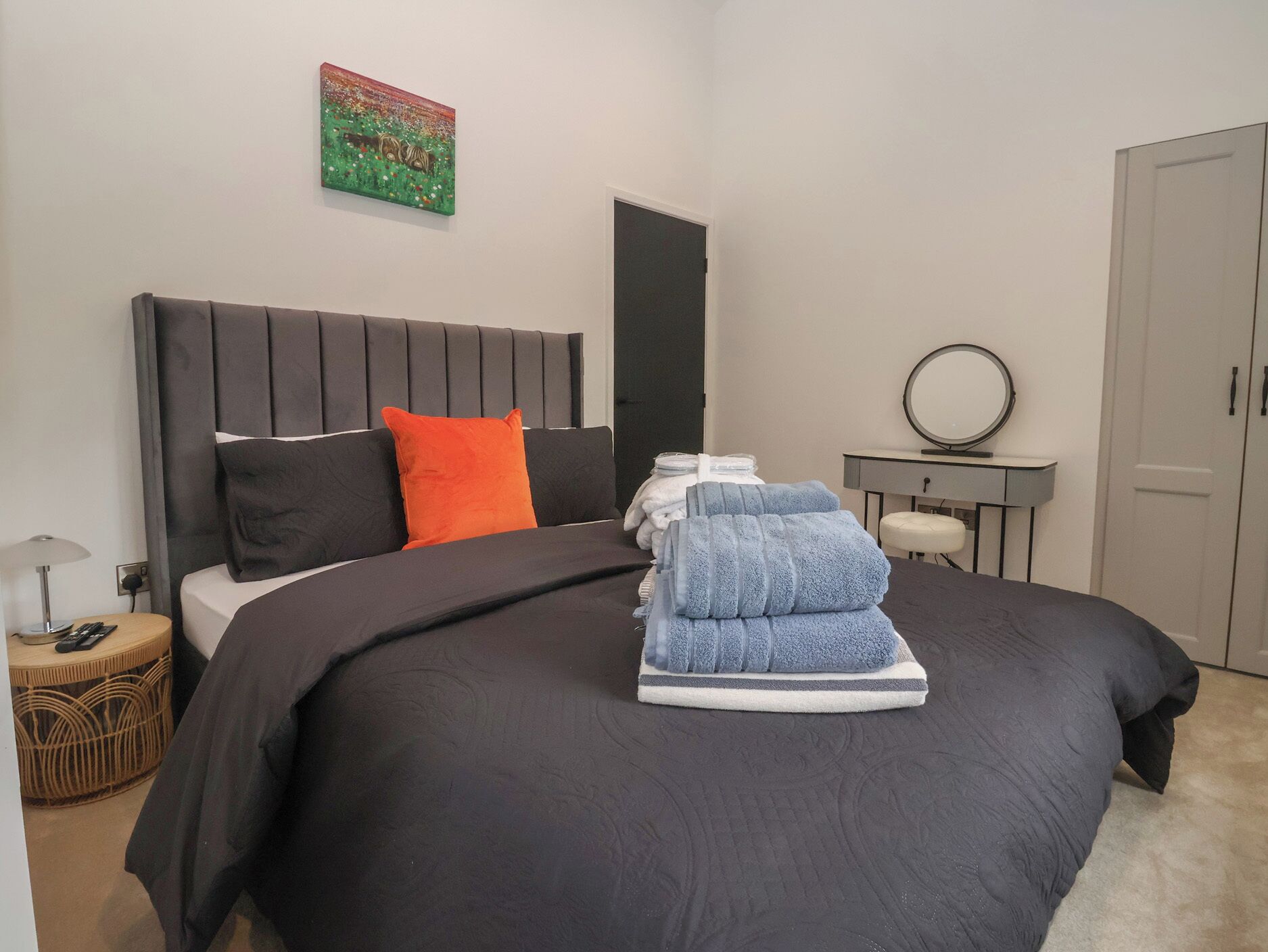 A neatly made bed with a black headboard, a single orange pillow, and a stack of folded towels.
