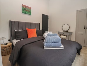 A neatly made bed with a black headboard, a single orange pillow, and a stack of folded towels. - Wood Cottage (Skipton)