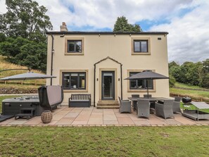 A two-story house with a patio area featuring outdoor furniture, a hot tub, and a barbecue grill. - Wood Cottage (Skipton)