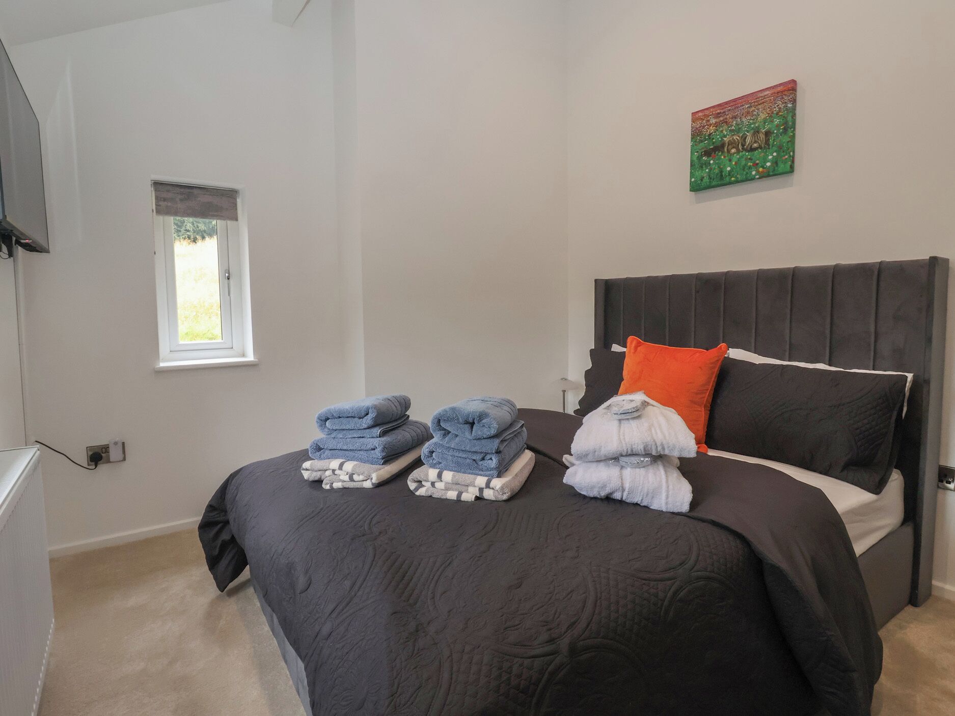 A bedroom with a bed, a window, a painting, and a wall socket.
