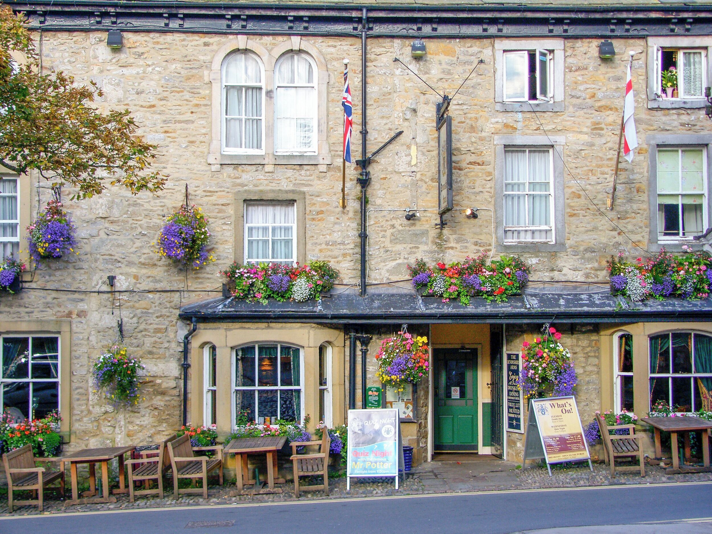 A stone building with flower boxes, outdoor seating, and flags.