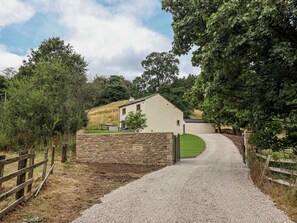 A gravel driveway leading to a stone wall with a sign reading 'Winterburn Wood House.' - Wood Cottage (Skipton)