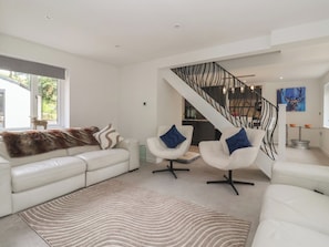 A modern living room with a white sofa, two white armchairs, a patterned rug, and a staircase with a metal railing. - Wood Cottage (Skipton)