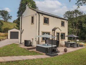 A two-story house with a patio area featuring outdoor furniture, a hot tub, and a covered seating area. - Wood Cottage (Skipton)