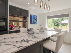 A modern kitchen with a marble countertop, pendant lighting, and a large window with a view of greenery. - Wood Cottage (Skipton)
