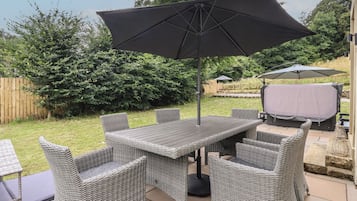 An outdoor patio with a table and chairs, a large umbrella, and a barbecue grill.