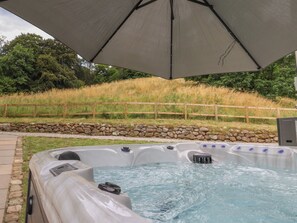 A hot tub under a canopy with a stone wall and wooden fence in the background. - Wood Cottage (Skipton)
