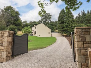 A gravel driveway leading to a house with a stone wall on one side and a metal gate. - Wood Cottage (Skipton)
