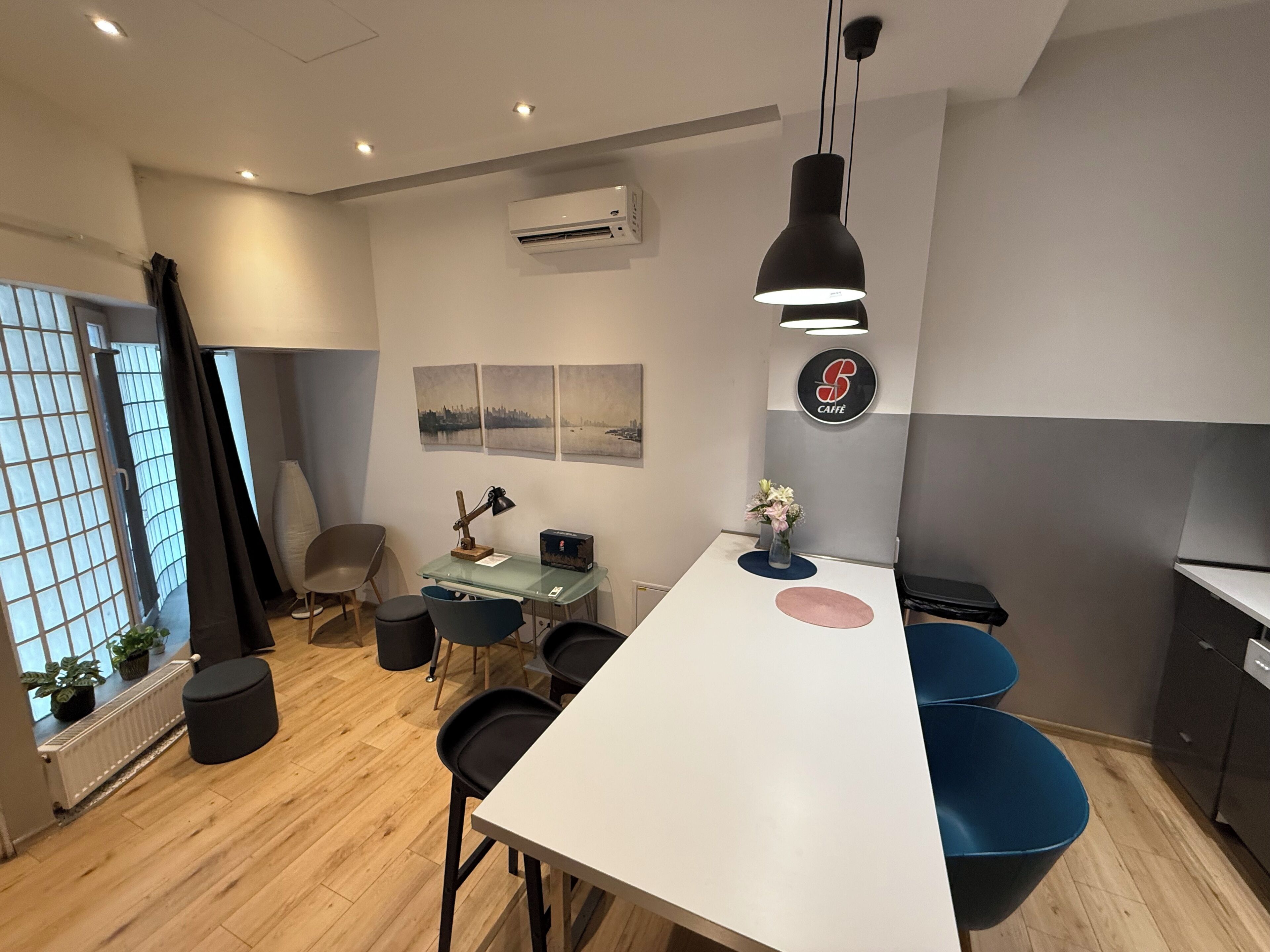 A modern office space with a white desk, black chairs, a glass table, and a hanging pendant light.