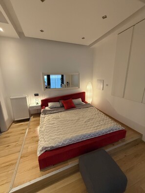 A bedroom with a bed, bedside table, lamp, radiator, and a mirror. - Modern studio downtown Budapest, next to airport road, also for business trips (Budapest)