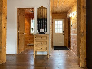 Ein Innenkorridor mit Holzboden, einer Kommode, einer Tür und einem Fenster mit Blick.
