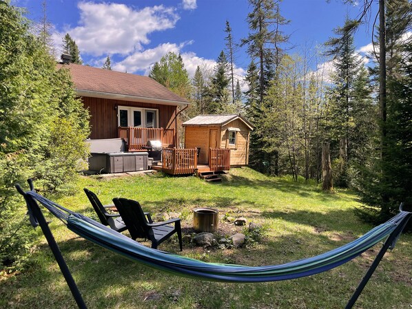 A cabin with a deck, a hot tub, and a hammock in a forested area. - Chalet NOX | Spa & Sauna | Romantic Getaway (Notre-Dame-de-la-Merci)