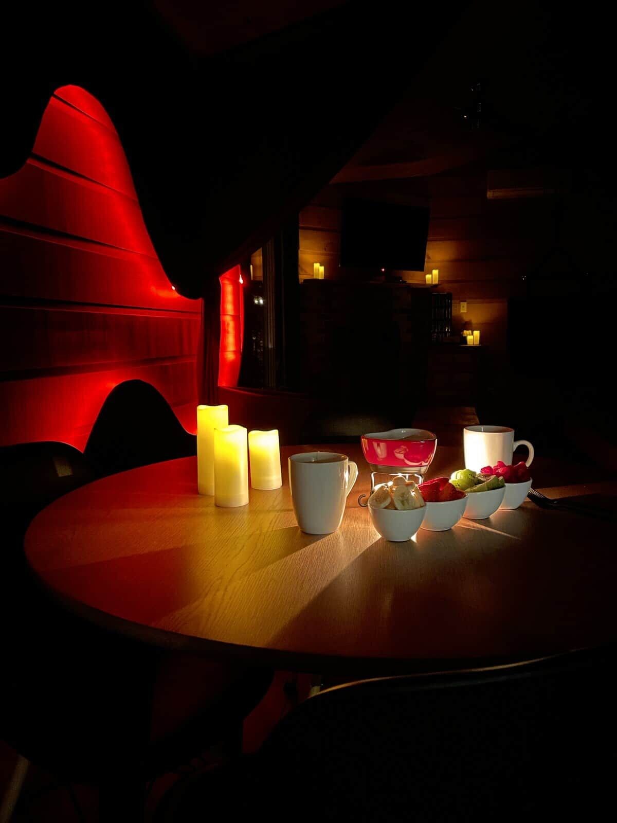 A dimly lit room with a round table, candles, and a red ambient light.