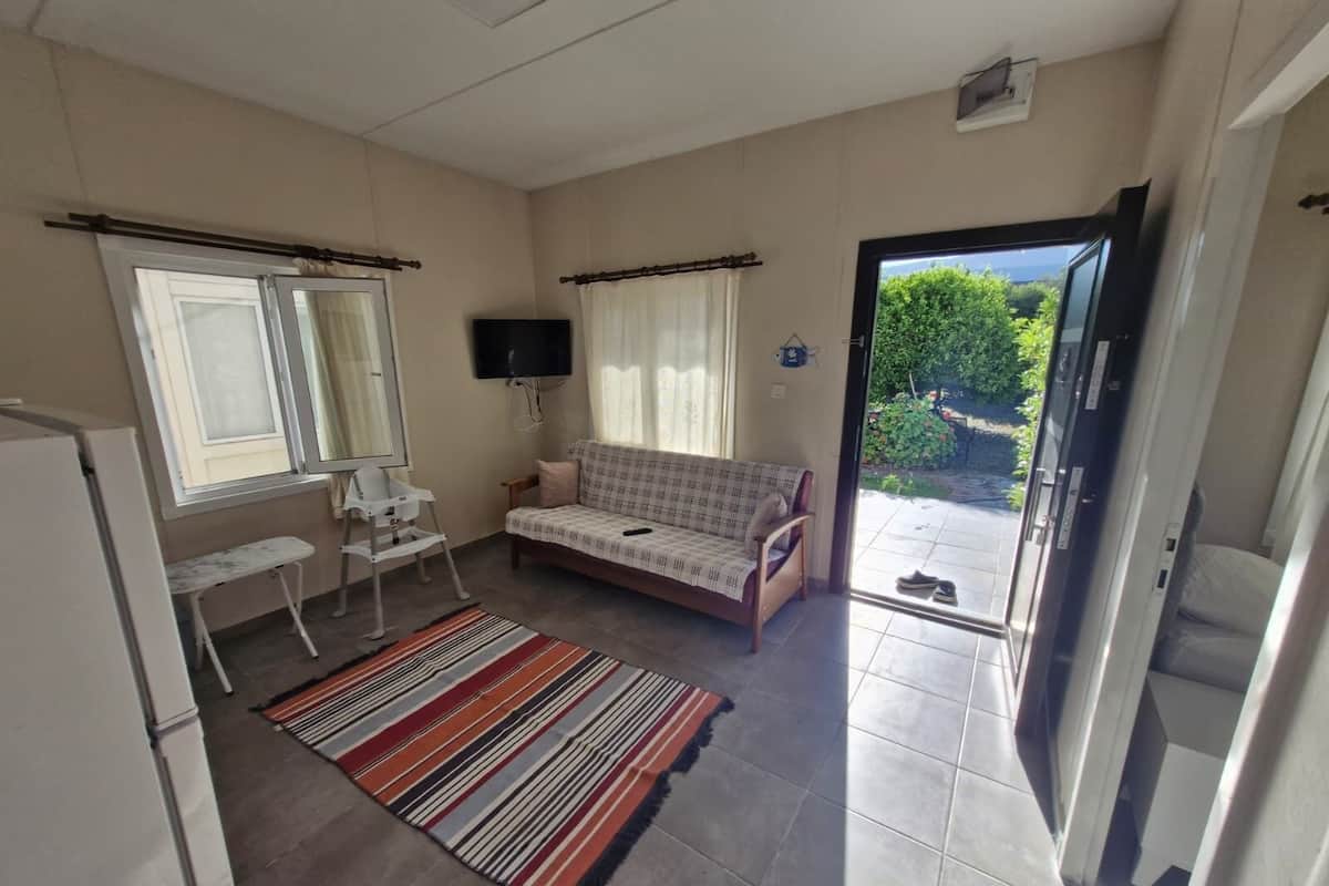 Un espacio habitable compacto con sofá, una mesita, televisor y puerta corredera que da a un balcón.