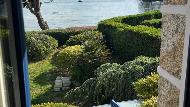 Vista de un jardín ajardinado con un cuerpo de agua, barcos y una costa distante.