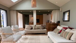 Amplia sala de estar con techo alto, un ventanal grande y una cocina al fondo.