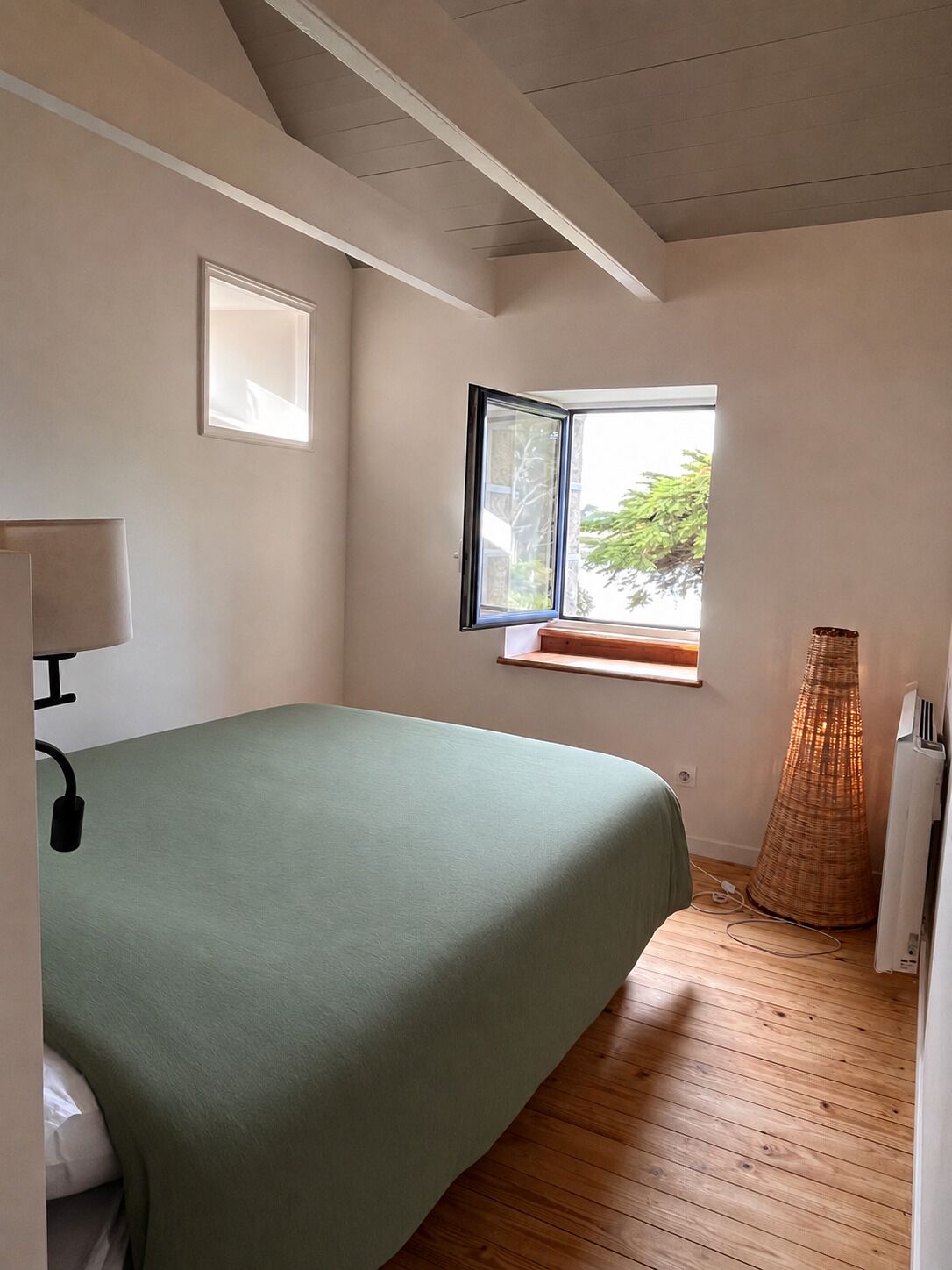 Een slaapkamer met een bed, een raam, een lamp en een lampenvoet van wilg.