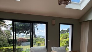 Un amplio salón con un ventanal grande, un sofá, dos sillones y una lámpara colgante.