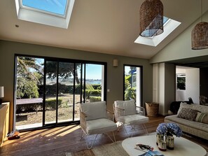 A spacious living room with a large sliding glass door leading to a garden, a sofa, a coffee table with decorative items, and a ceiling skylight.