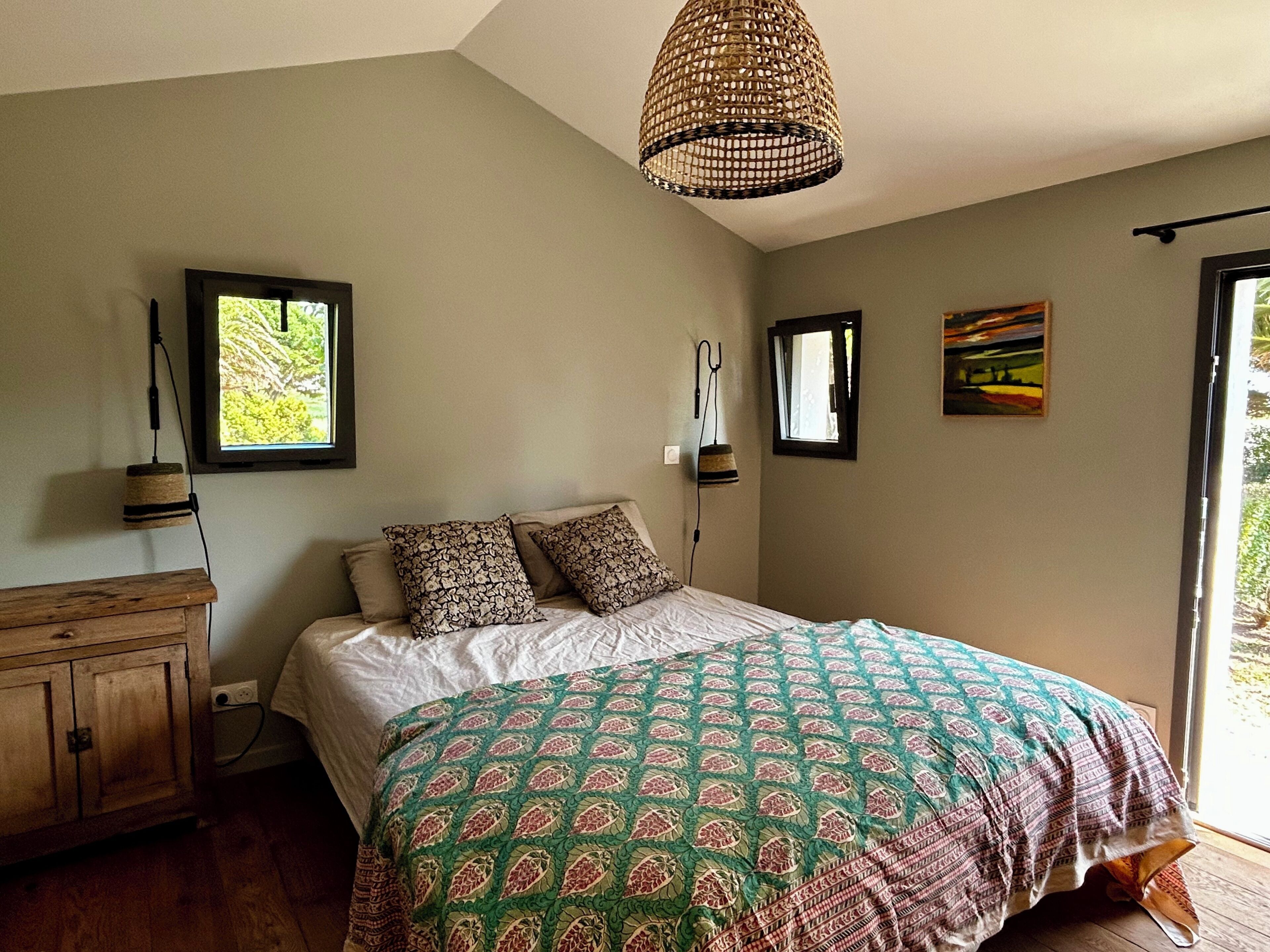 A bedroom with a bed, a wooden dresser, a hanging light fixture, and a window.