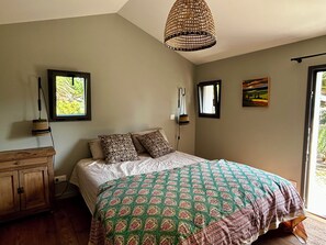 Un dormitorio con una cama, un aparador de madera, una lámpara colgante y una ventana.