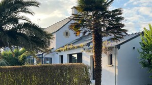 Un edificio blanco con techo inclinado, una ventana visible y una palmera en primer plano.