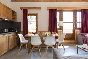 A cozy kitchen with wooden cabinets, a dining table with chairs, and a window with curtains.