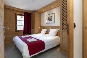 A wooden-paneled room with a bed, a window with red curtains, and a framed picture on the wall.