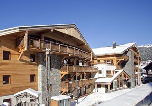 A multi-story wooden building with balconies, stone pillars, and a snowy landscape.