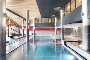 A modern indoor swimming pool with lounge chairs, a red wall, and a stone wall.