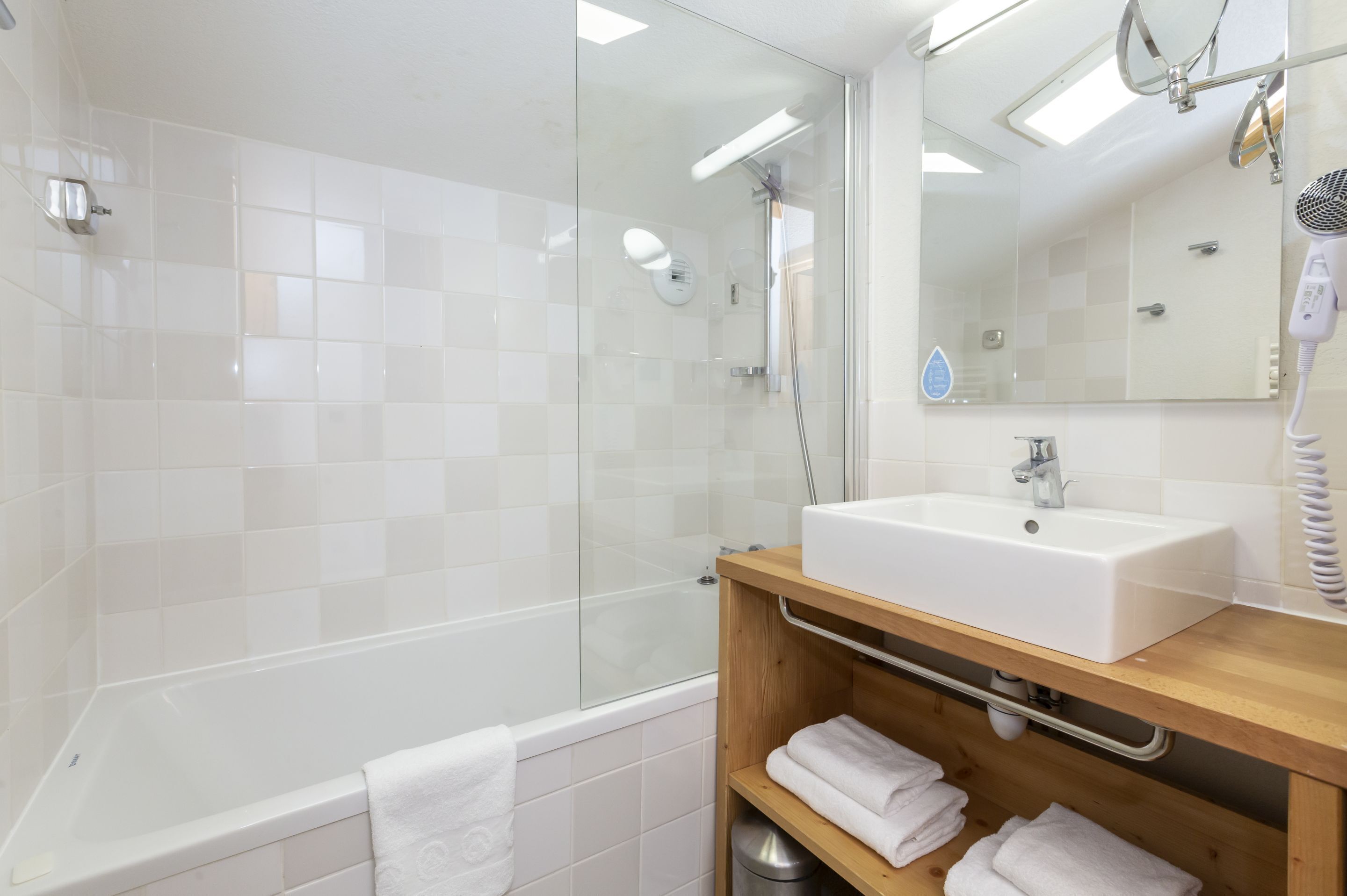 Une salle de bain moderne avec une douche à parois de verre, un lavabo blanc et un meuble-lavabo en bois.