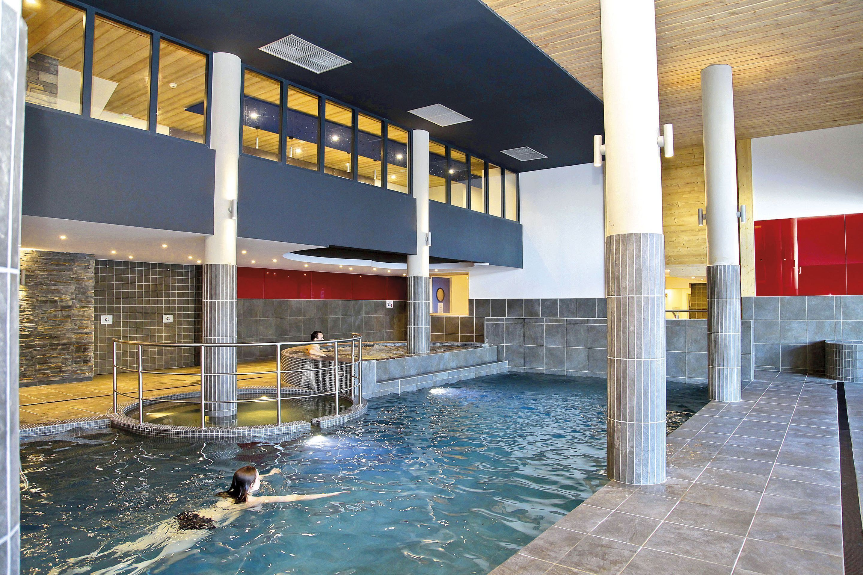 En indendørs swimmingpool med en person, et niveau med vinduer og en rød væg.